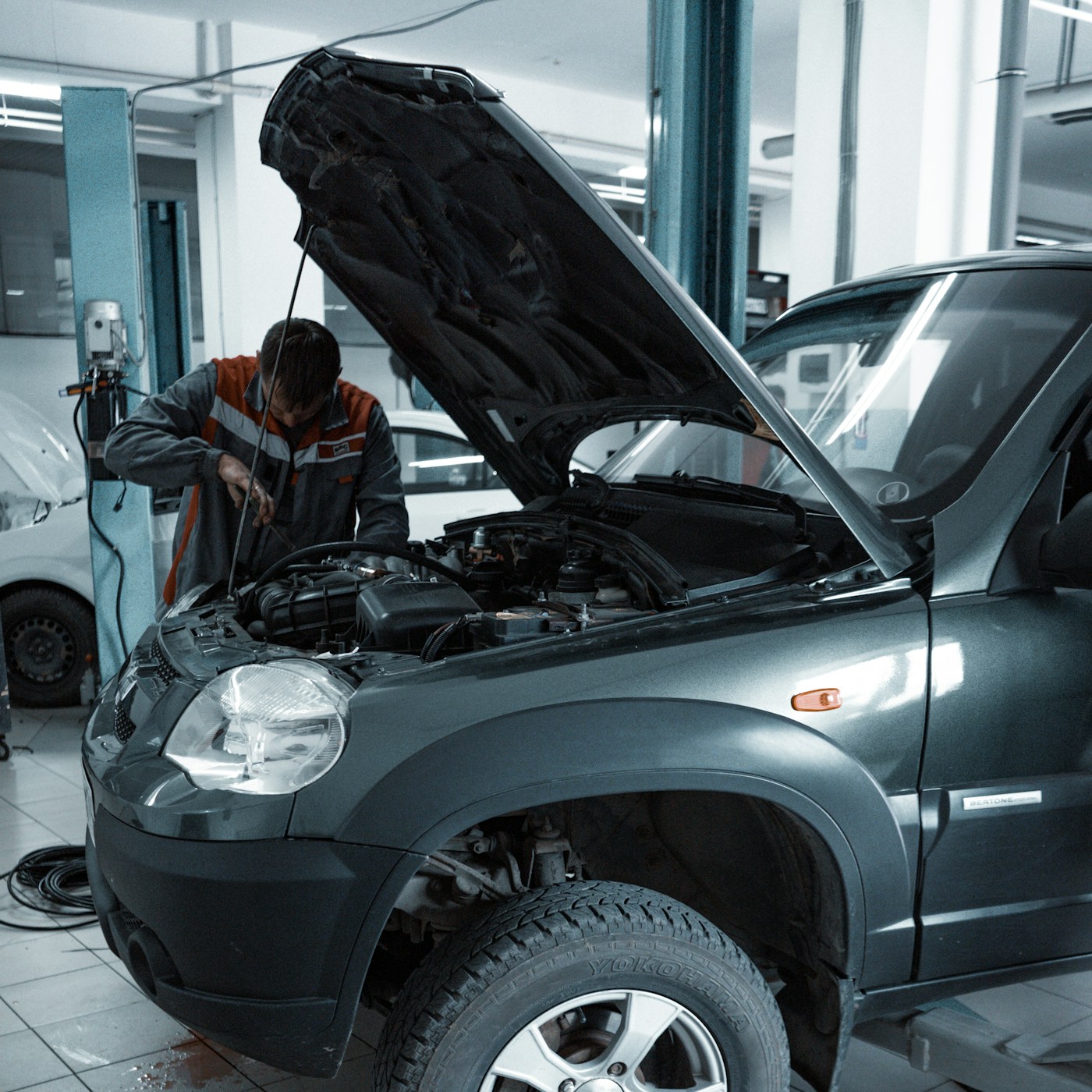 Mechaniker in Arbeitskleidung am geöffneten Motorraum eines SUV