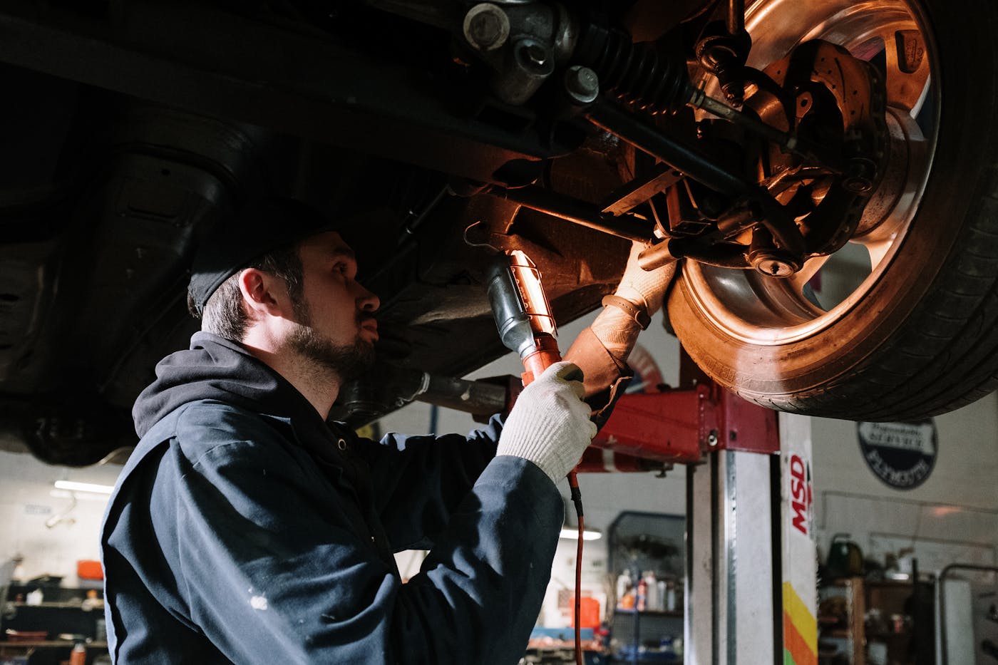 Mechaniker inspiziert Fahrzeugboden mit Werkstattlampe unter dem Auto